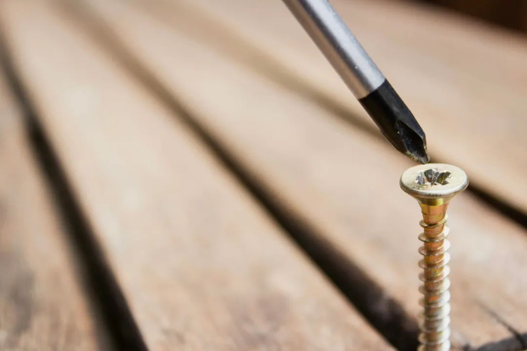 A hand turning a screwdriver in a screw on a wooden surface