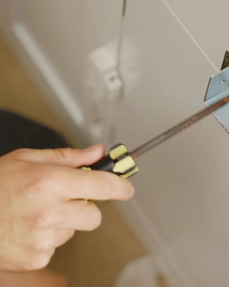 A hand turning a screwdriver into a cabinet bracket