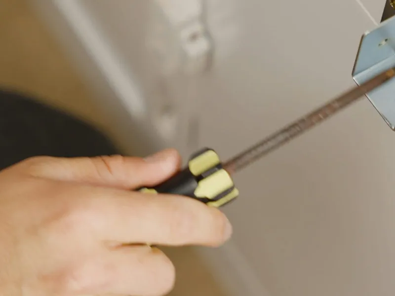 A hand driving a screw into a wall plate