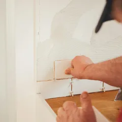 Hands setting a tile on a wall