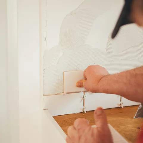 Hands setting a tile on a wall