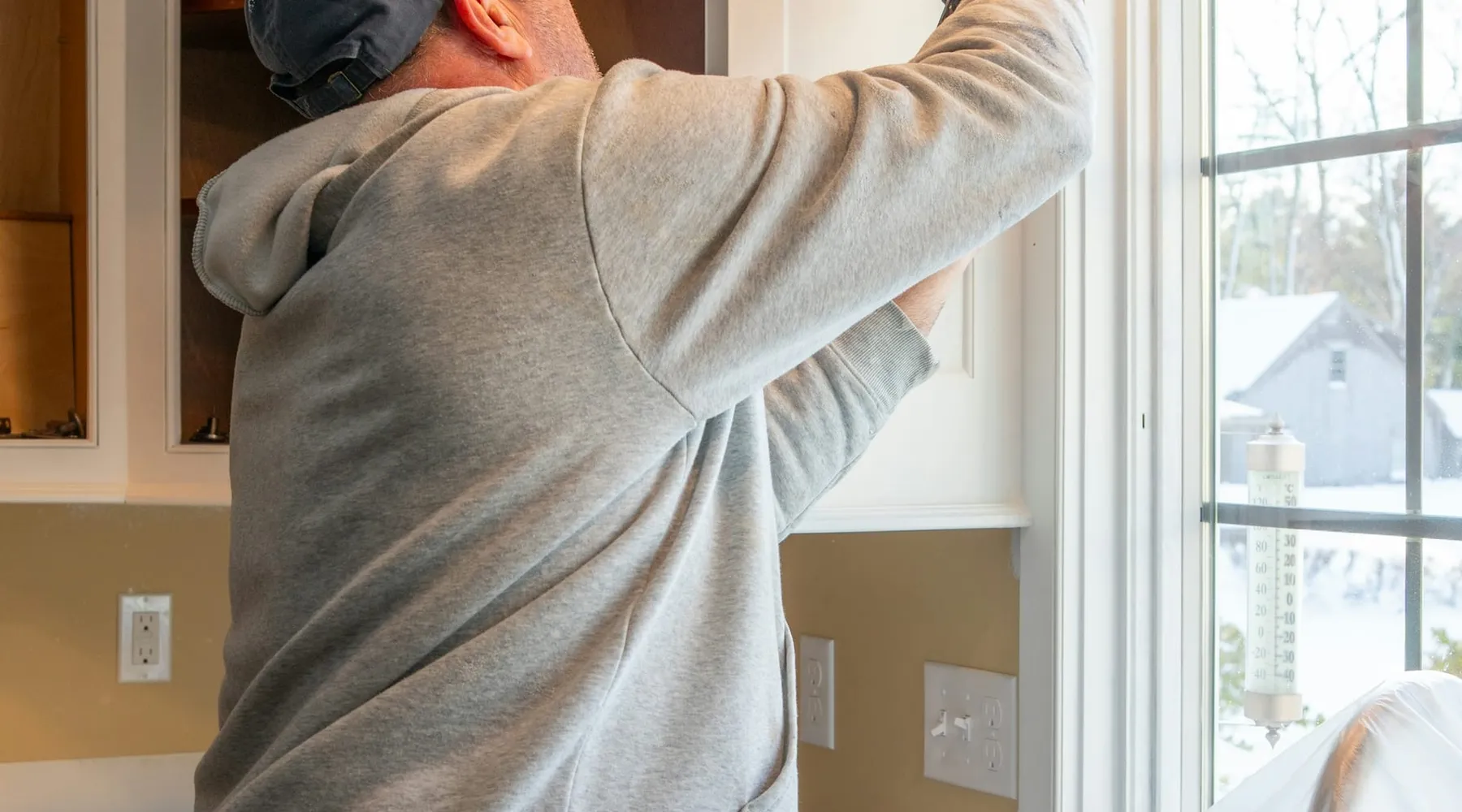 A handyman sealing a kitchen cabinet by a bright window
