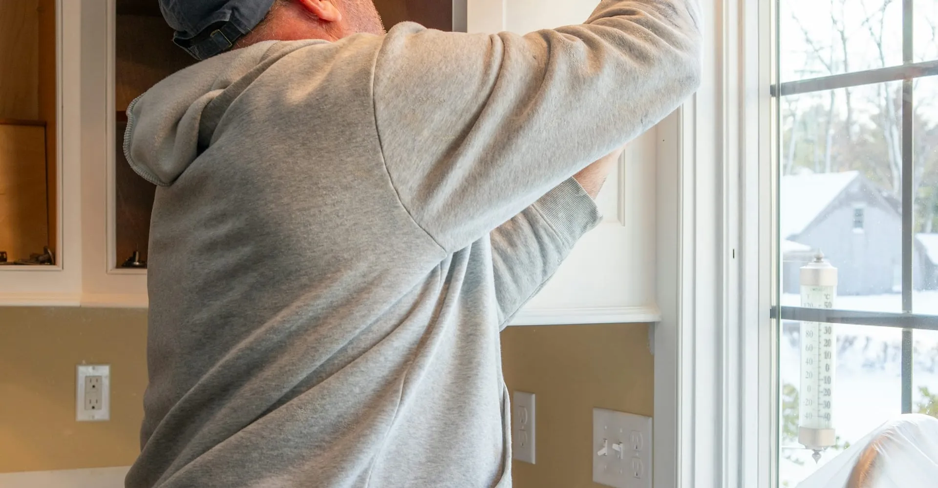 A handyman sealing a kitchen cabinet by a bright window