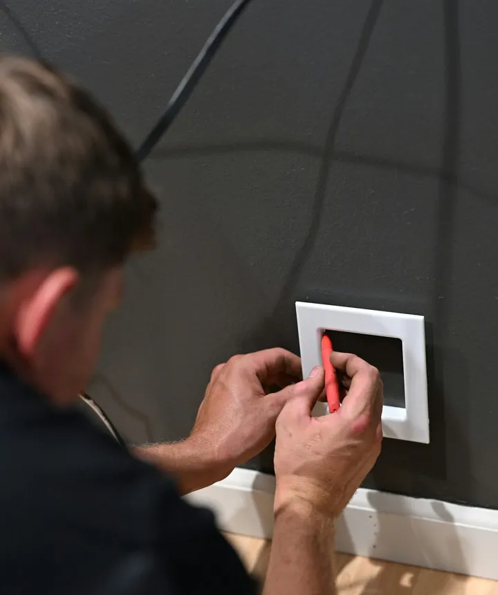 A handyman fitting a new switch plate on a dark wall