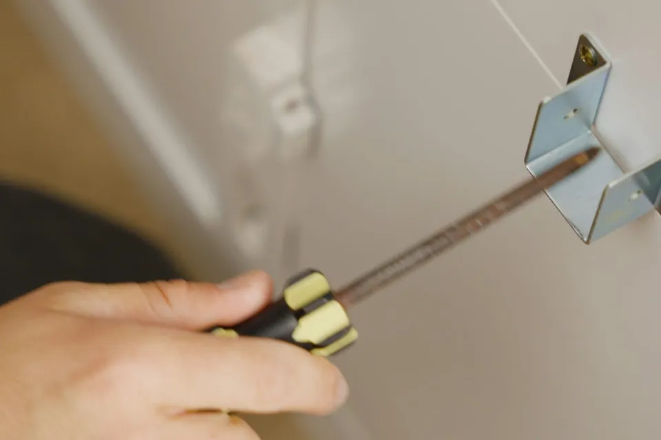 A hand driving a screw into a cabinet bracket