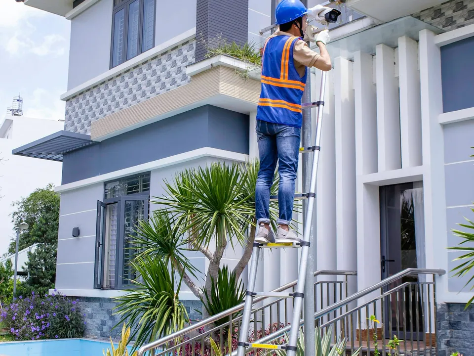 A crew member on a ladder working on the front of a family house