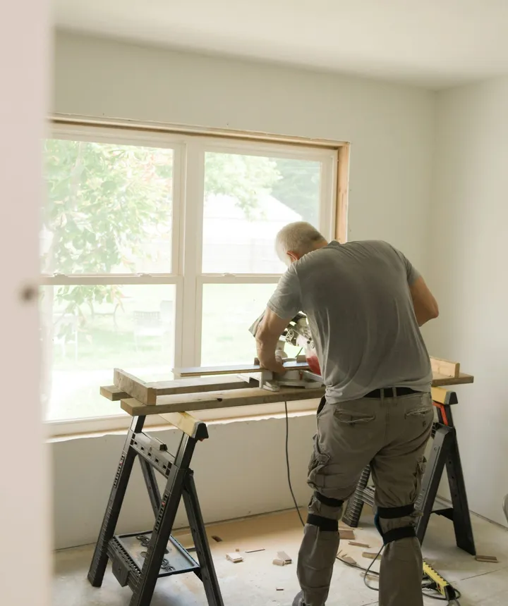 A crew member cutting trim at a saw bench by a sunny window