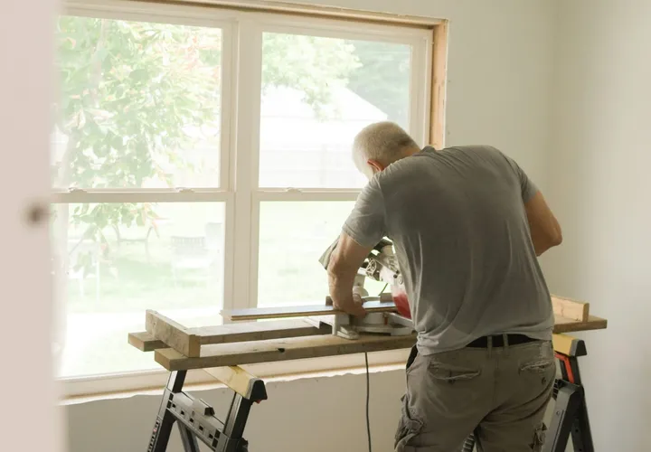 A crew member cutting trim at a saw bench by a sunny window