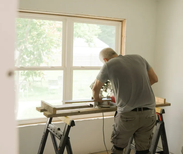 A crew member cutting trim at a saw bench by a sunny window