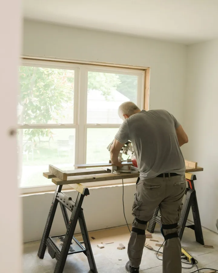 A crew member cutting trim at a saw bench by a sunny window