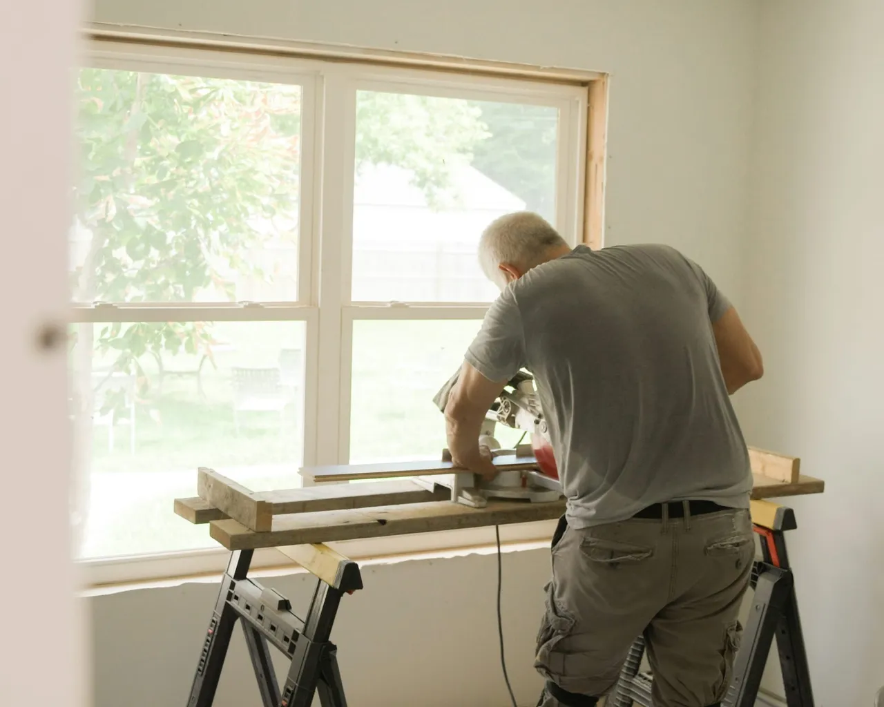 A crew member cutting trim at a saw bench by a sunny window