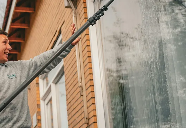 A smiling window cleaner washing a window with a water-fed pole