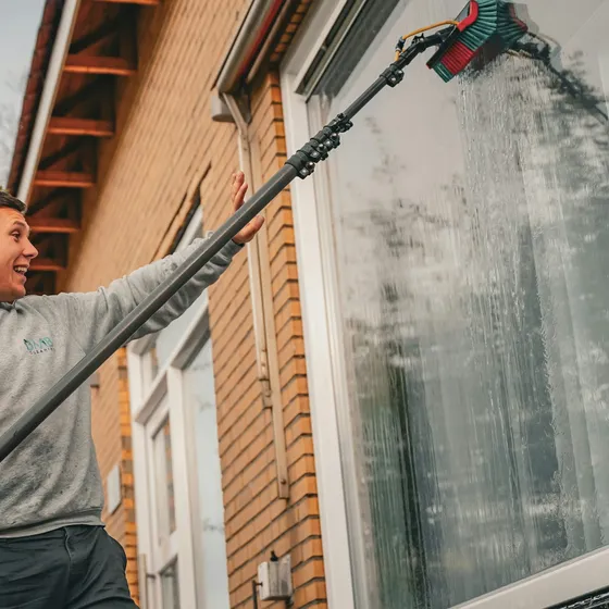 A smiling window cleaner washing a window with a water-fed pole